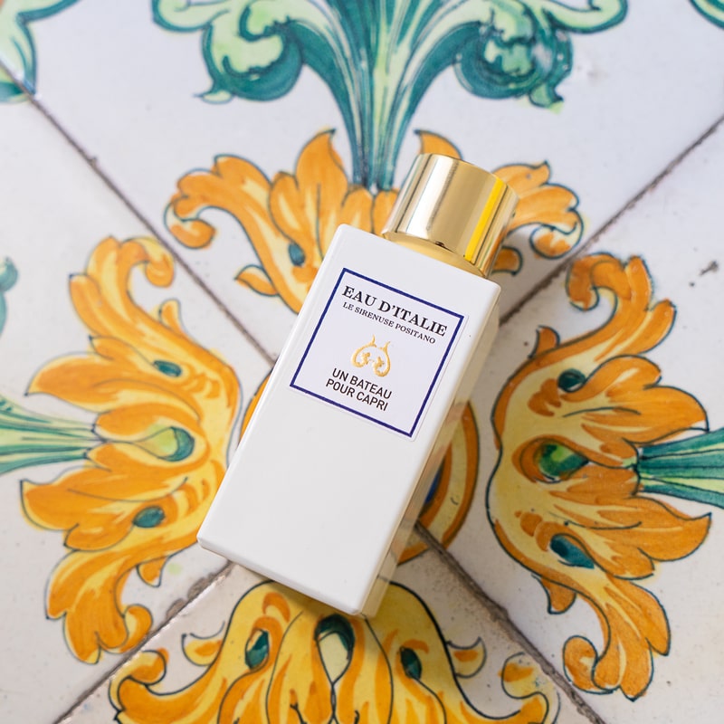 Lifestyle shot top view of Eau d'Italie Un Bateau Pour Capri Eau de Parfum Spray (100 ml) on tile with yellow flowers