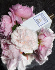Lifestyle shot top view of Eau d'Italie Un Bateau Pour Capri Eau de Parfum Spray (100 ml) with pink flowers in the background