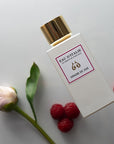 Lifestyle shot top view of Eau d'Italie Graine de Joie Eau de Parfum Spray (100 ml) with raspberries and single pink flower in the background