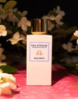 Lifestyle shot of Eau d'Italie Rosa Greta Eau de Parfum Spray bottle (100 ml) on pink textured fabric and white flowers in the background