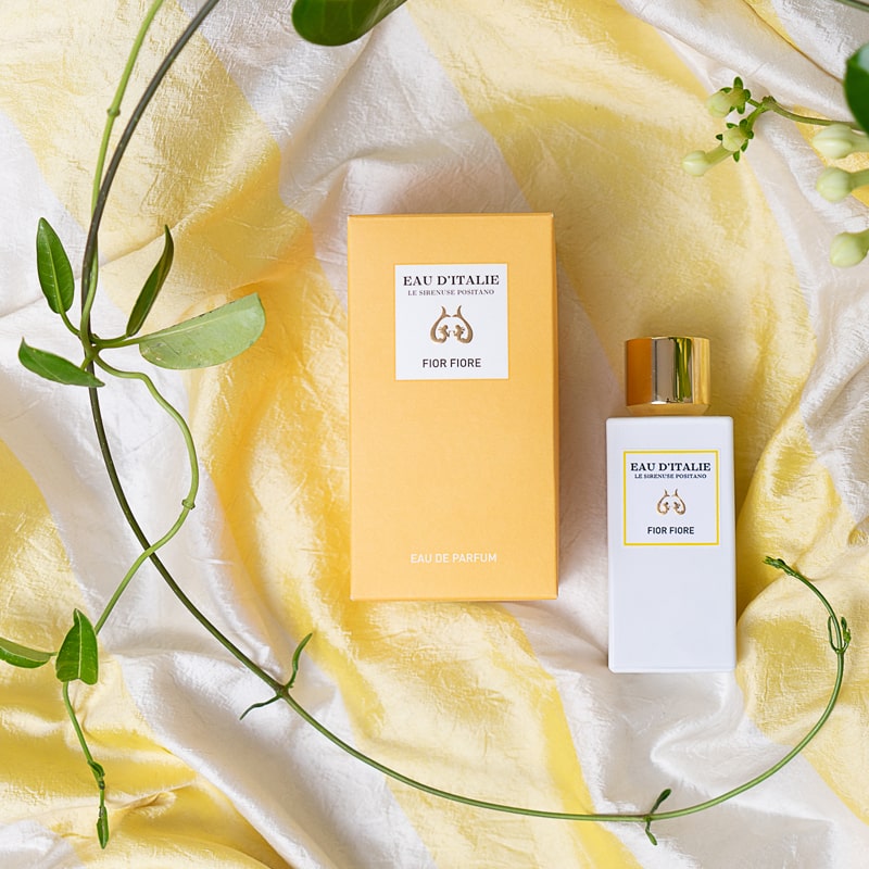 Lifestyle shot top view of Eau d'Italie Fior Fiore Eau de Parfum Spray (100 ml) with box and delicate green branch in the background