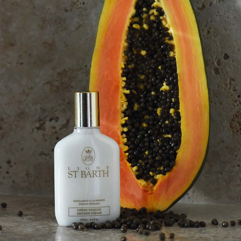 Lifestyle shot of Ligne St. Barth Papaya Peeling Shower Cream 4.2 oz with half of a papaya in the background and papaya seeds in the foreground