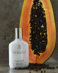 Lifestyle shot of Ligne St. Barth Papaya Peeling Shower Cream 4.2 oz with half of a papaya in the background and papaya seeds in the foreground