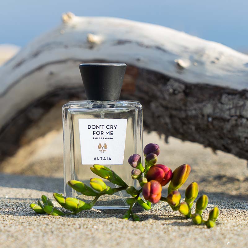 Beauty shot of ALTAIA Don't Cry For Me Eau de Parfum on a beach with wood in the background and flowers in the foreground