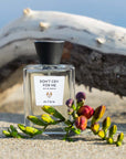 Beauty shot of ALTAIA Don't Cry For Me Eau de Parfum on a beach with wood in the background and flowers in the foreground