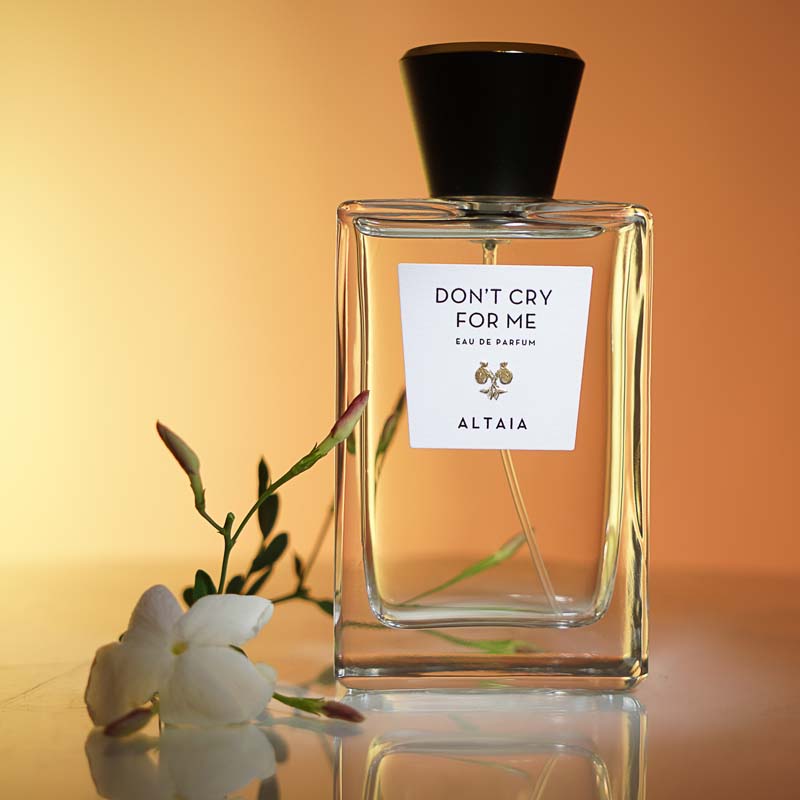 Beauty shot of ALTAIA Don&#39;t Cry For Me Eau de Parfum with white flower in the foreground and orange background
