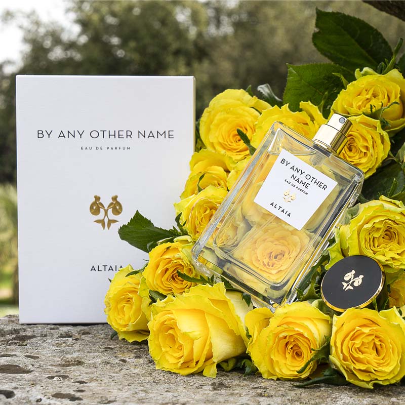 Beauty shot of ALTAIA By Any Other Name Eau de Parfum nestled in a bouquet of yellow roses and box in the background