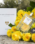 Beauty shot of ALTAIA By Any Other Name Eau de Parfum nestled in a bouquet of yellow roses and box in the background