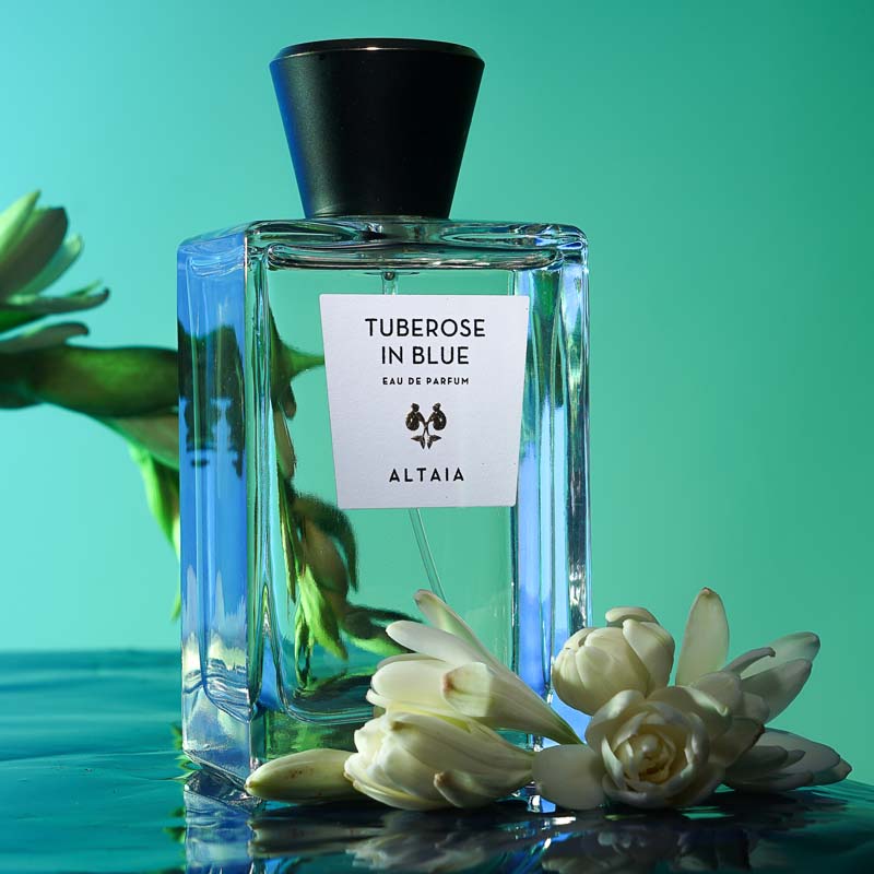 Beauty shot of ALTAIA Tuberose in Blue Eau de Parfum with top off and tuberose flowers in the background and foreground