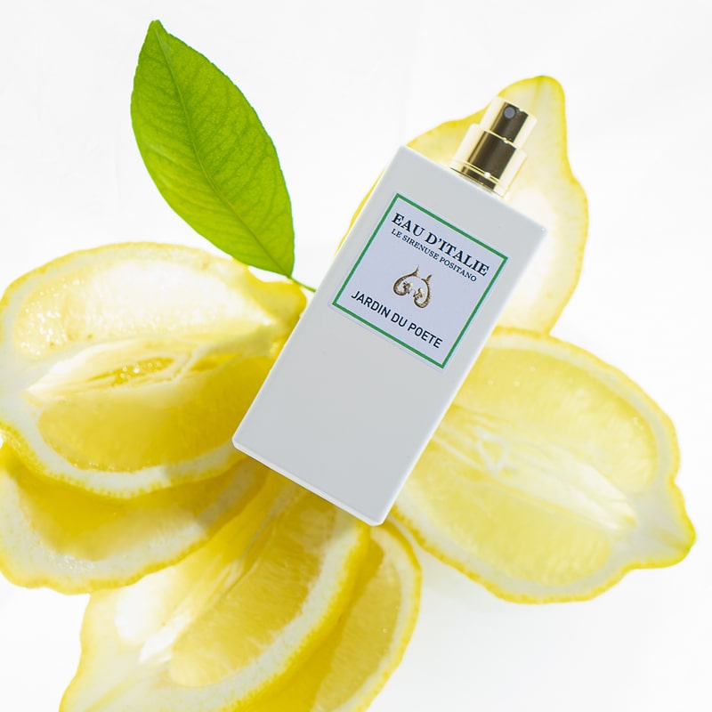 Lifestyle shot top view of Eau d'Italie Jardin du Poete Eau de Parfum Spray (100 ml) with lemons and single green leaf in the background