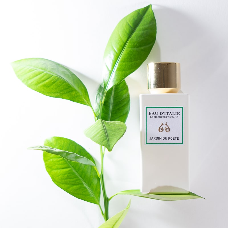Lifestyle shot of Eau d'Italie Jardin du Poete Eau de Parfum Spray (100 ml) with green leaves in the background