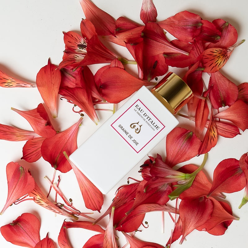 Lifestyle shot top view of Eau d'Italie Graine de Joie Eau de Parfum Spray (100 ml) with red flower petals in the background