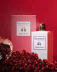 Lifestyle shot of Eau d'Italie Graine de Joie Eau de Parfum Spray (100 ml) with box and pomegranate and seeds in the foreground