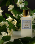 Lifestyle shot of Eau d'Italie Rosa Greta Eau de Parfum Spray bottle (100 ml) with white flowers in the background