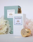 Lifestyle shot of Eau d'Italie Easy to Love Eau de Parfum Spray (100 ml) with box cap off and pale pink and cream flowers in the background and foreground