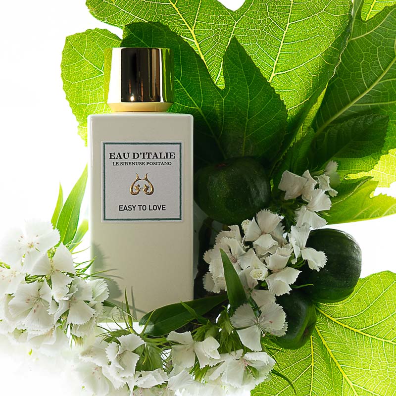 Lifestyle shot top view of Eau d&#39;Italie Easy to Love Eau de Parfum Spray (100 ml) with white flowers and large green leaves in the background