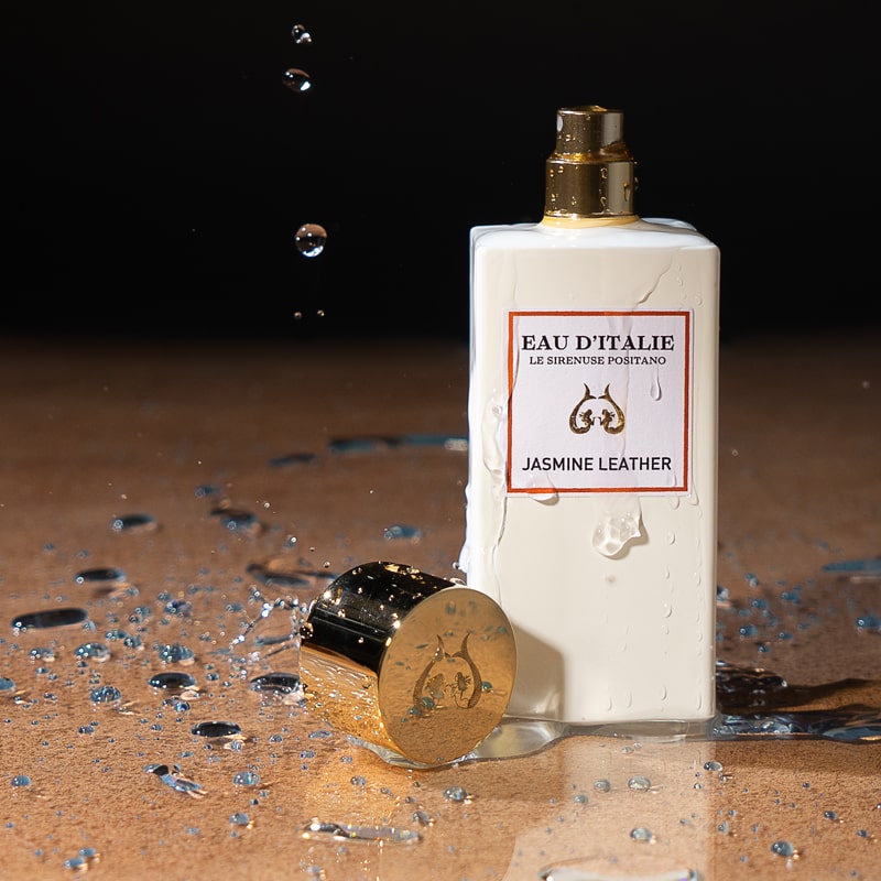 Lifestyle shot of Eau d'Italie Jasmine Leather Eau de Parfum Spray (100 ml) with cap off and water splash next to bottle