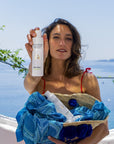Lifestyle shot of model holding Eau d'Italie Body Milk (200 ml) with the bay of Positano in the background