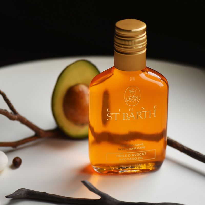 Beauty shot of Ligne St. Barth Avocado Oil 200 ml with half of an avocado and twig in the background