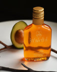 Beauty shot of Ligne St. Barth Avocado Oil 200 ml with half of an avocado and twig in the background